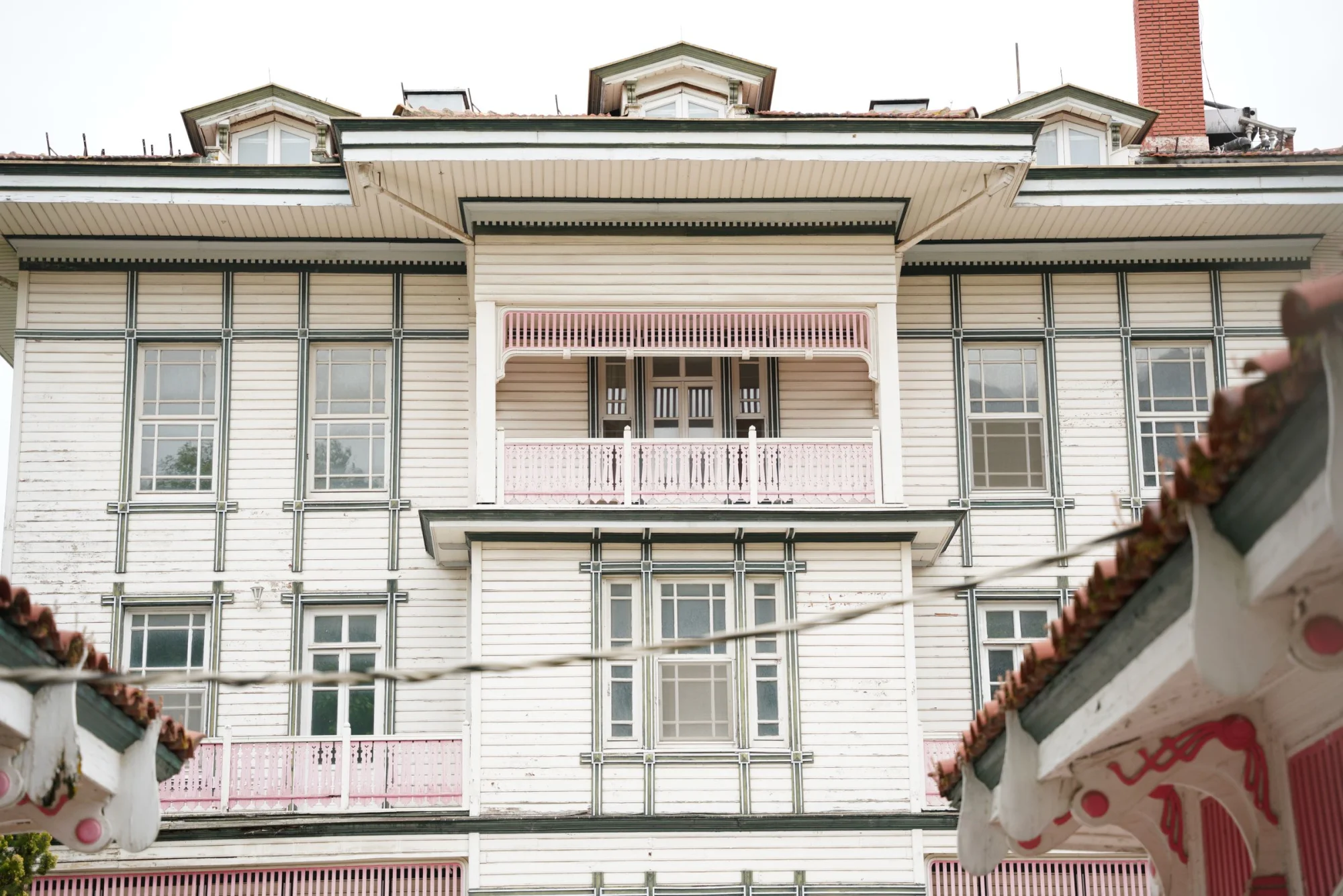 Stately white mansion featuring classic design elements and pink accents, full of windows and balconies.
