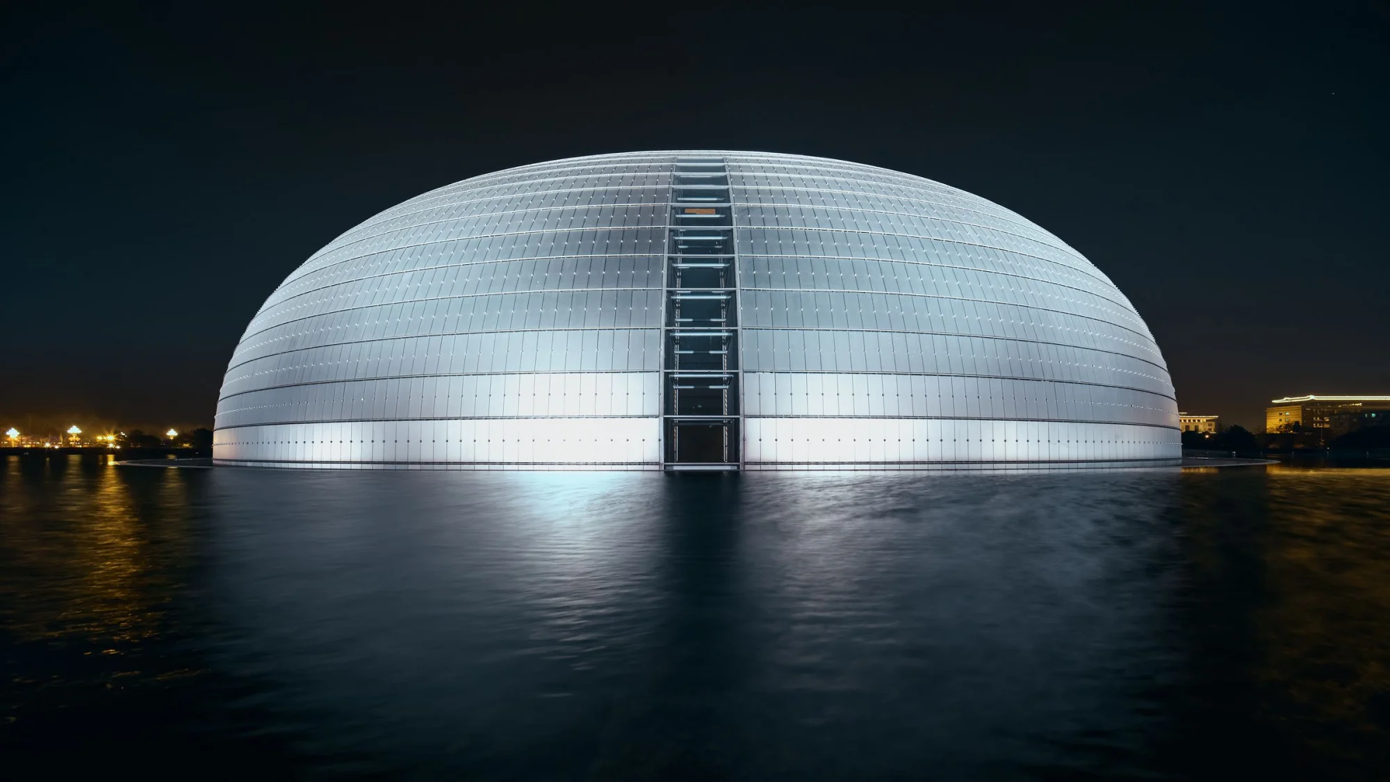 Dome-shaped National Centre for the Performing Arts reflecting on water at night.
