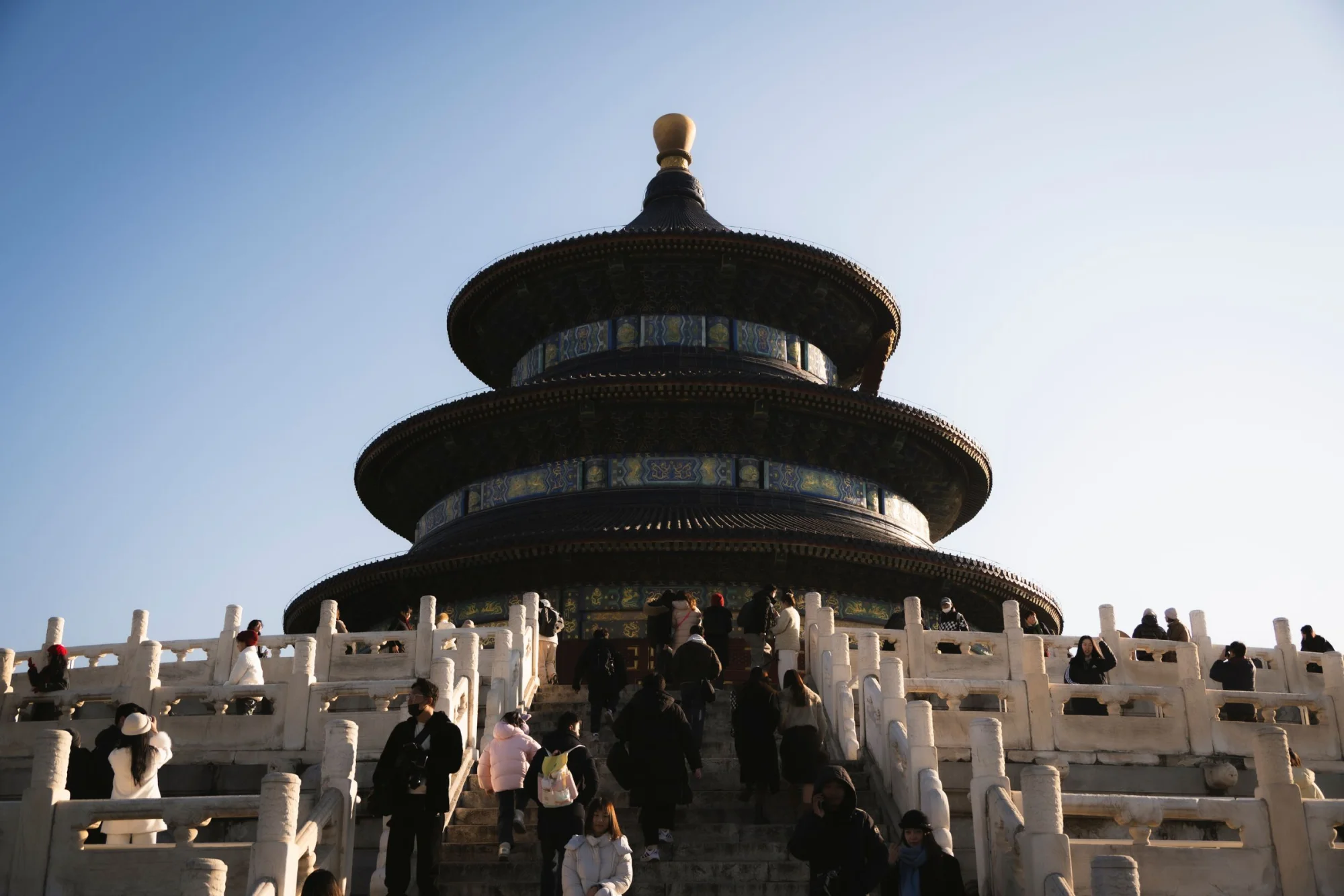 Visitors climbing the steps of the iconic Temple of Heaven in Beijing, capturing its grandeur under clear daylight.