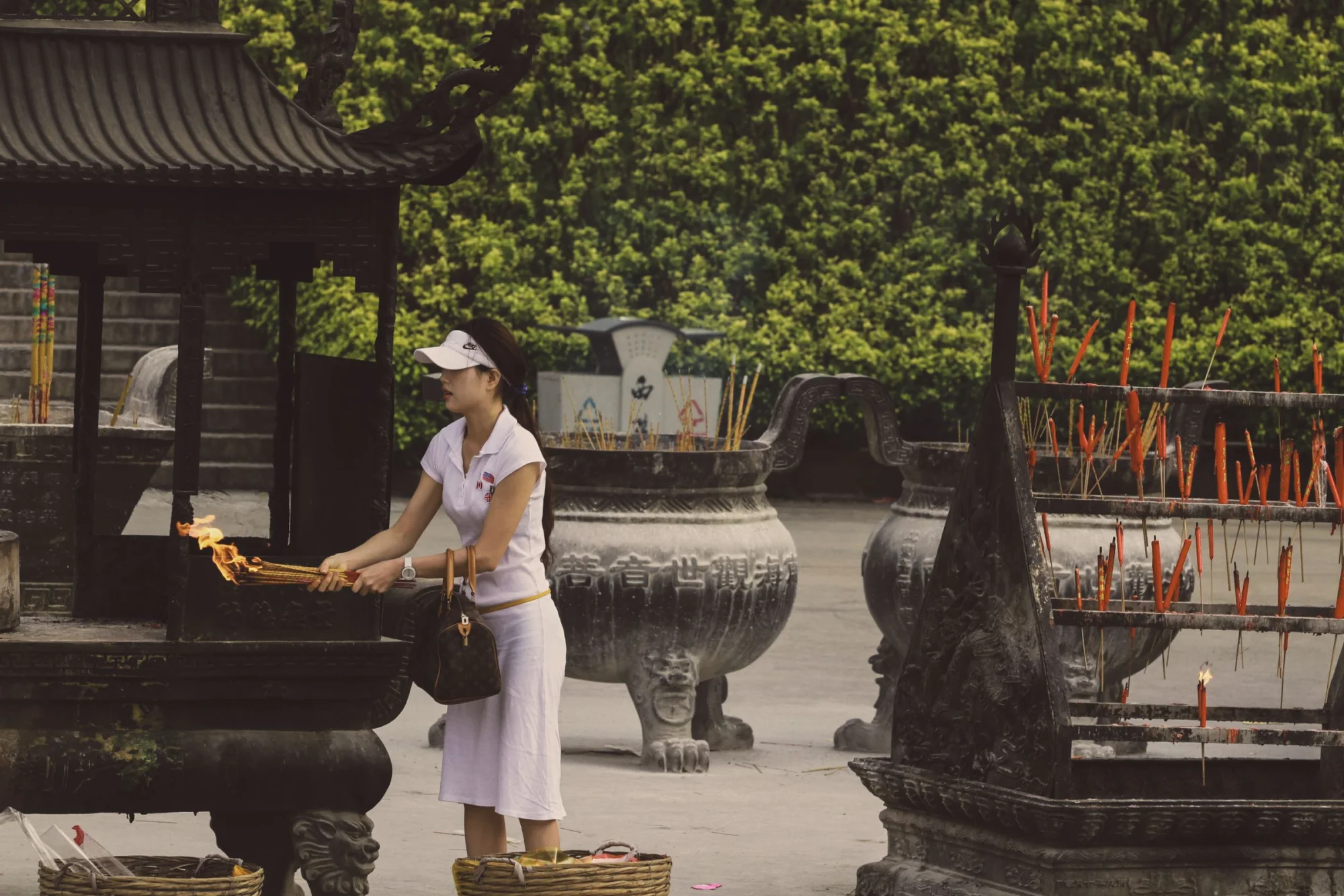 An Asian woman lights incense sticks at an outdoor temple shrine, embracing tradition and culture.