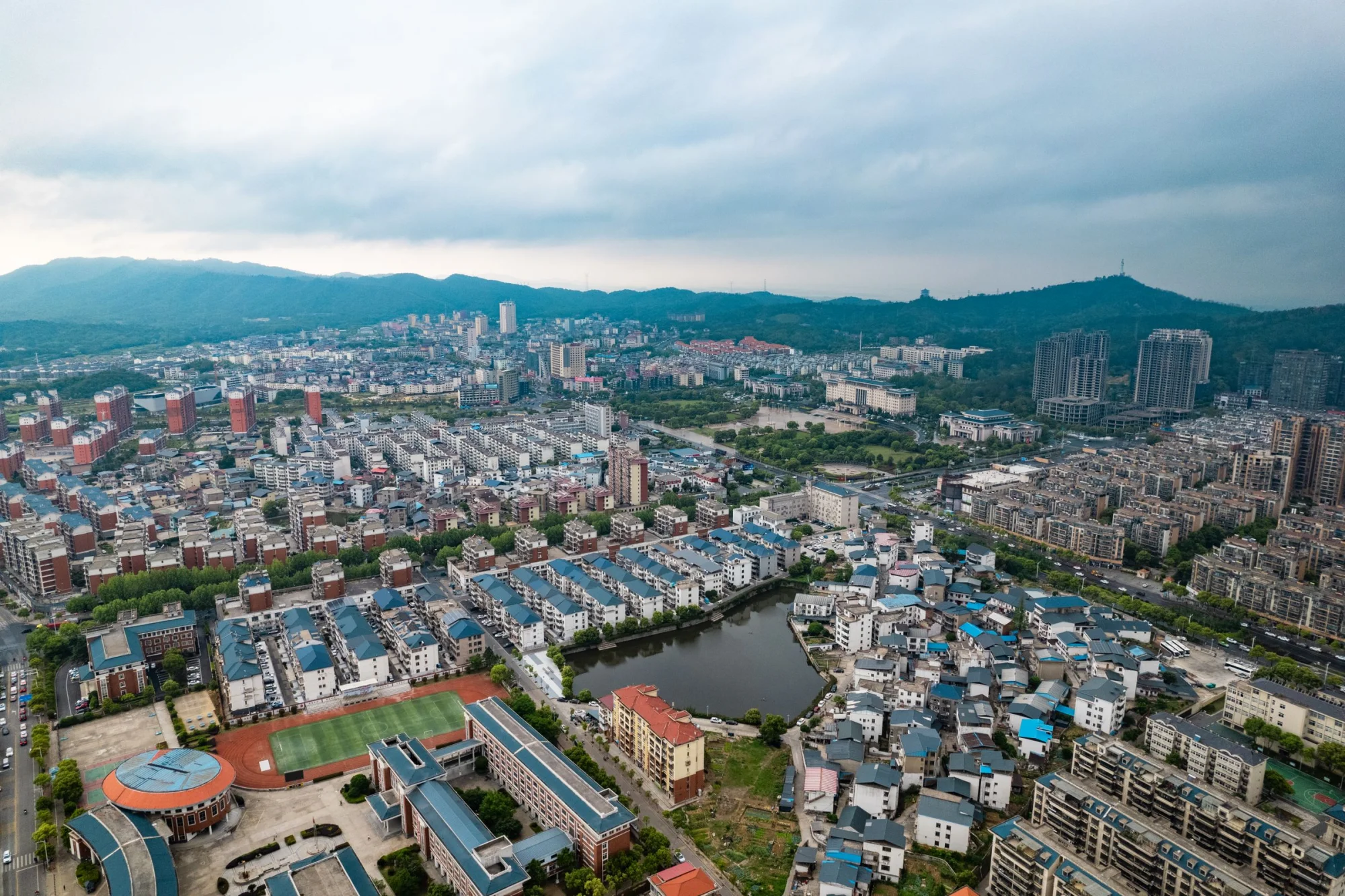 High-angle view of a suburban cityscape with residential buildings, sports fields, and distant mountains in China.