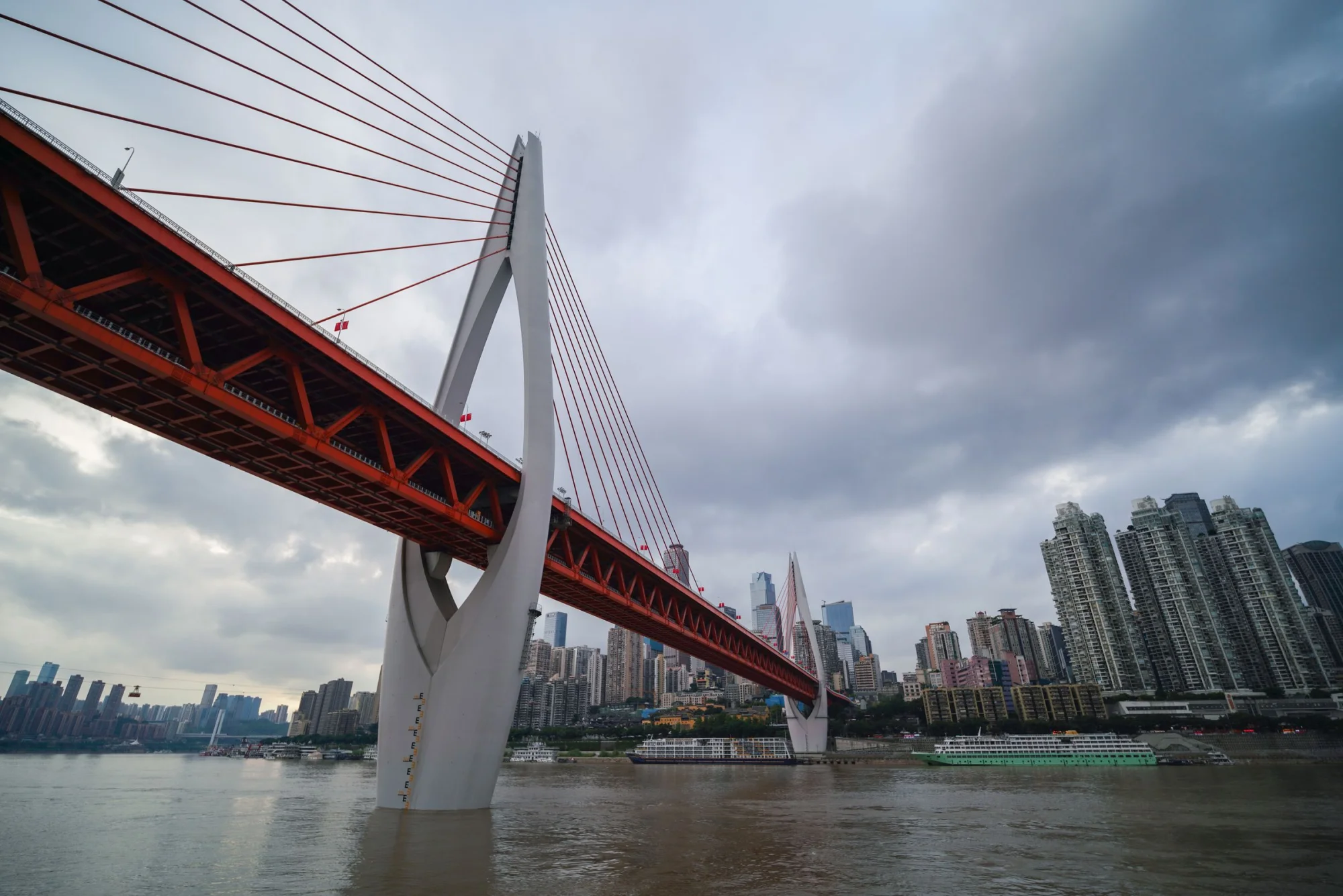 Scenic view of Dongshuimen Bridge spanning the Yangtze River in Chongqing, surrounded by a modern urban skyline.
