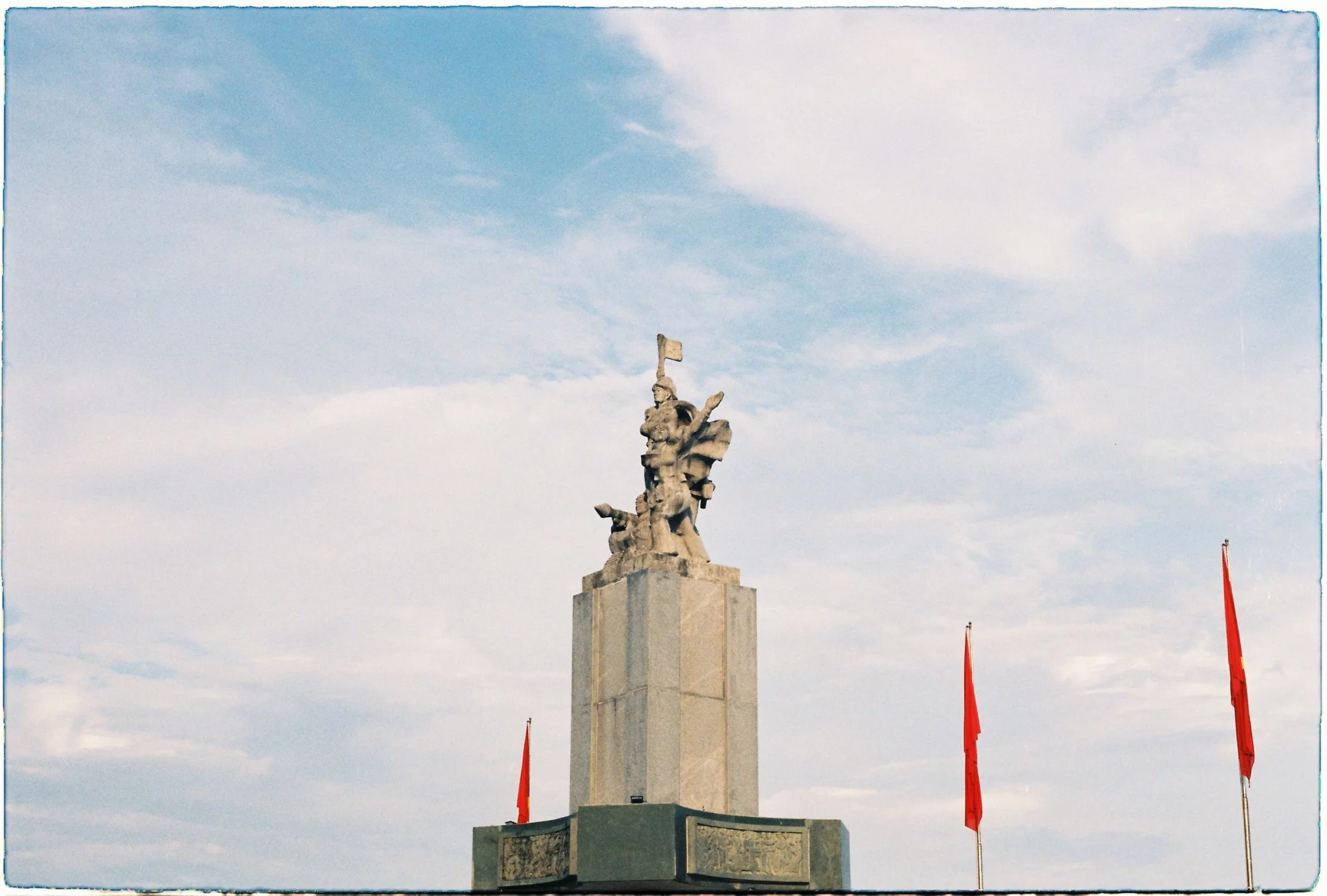 A grand monument standing tall against a clear blue sky with red flags waving.