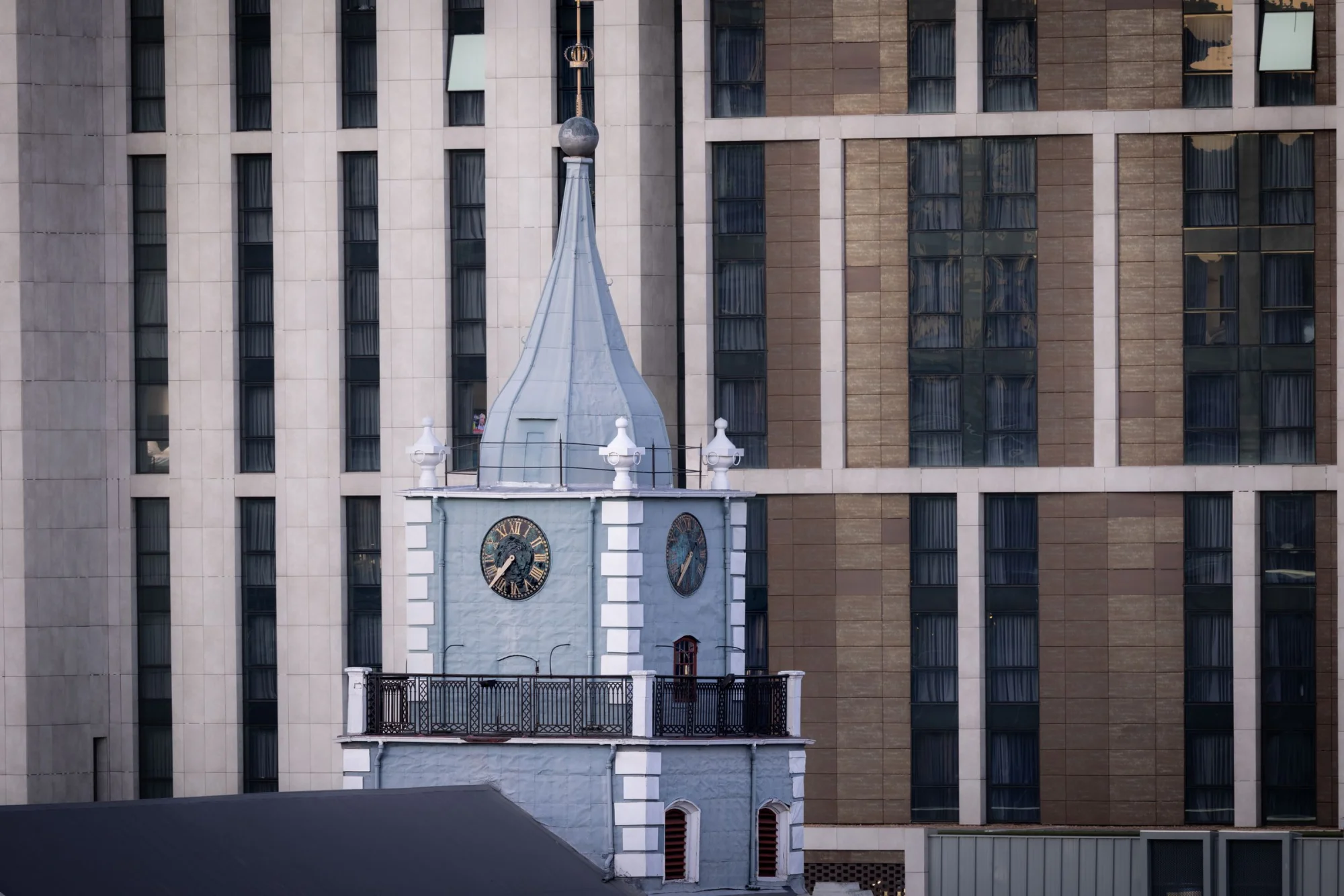 A historic clock tower stands contrastingly against a modern skyscraper facade.