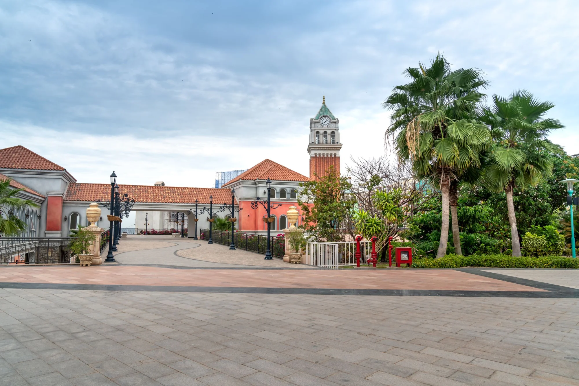 Charming European-style town square with clock tower, tiled roofs, and lush palm trees.