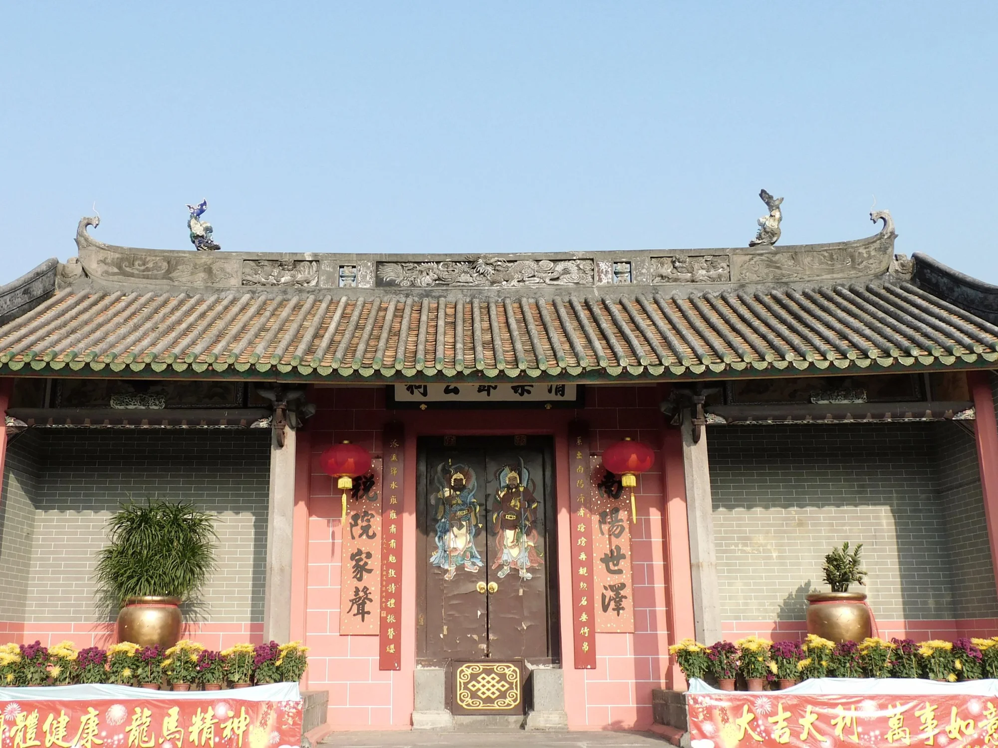 Exterior of ancient Buddhist Tang Ching Lok ancestral hall with hieroglyphs near ornamental doors and potted plant against cloudless blue sky in Hong Kong