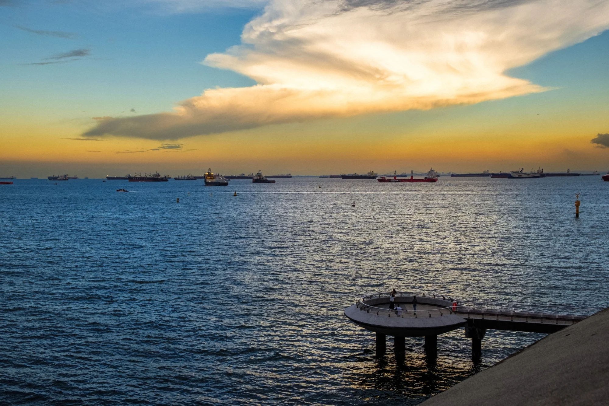 Beautiful sunset over a busy Singapore wharf with ships and a scenic pier view.