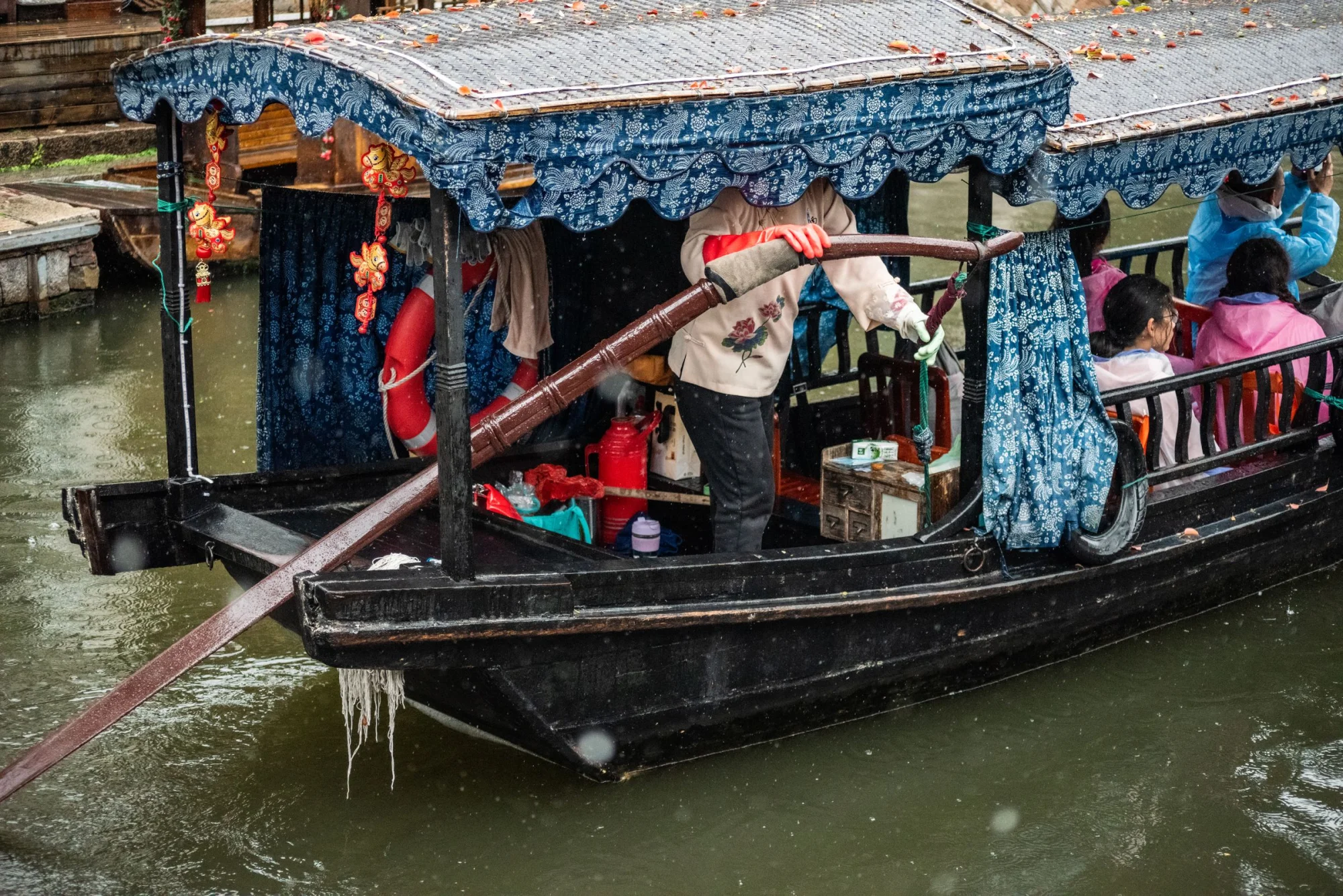 A vibrant scene of people on a traditional boat with patterned covers during a rainy day.