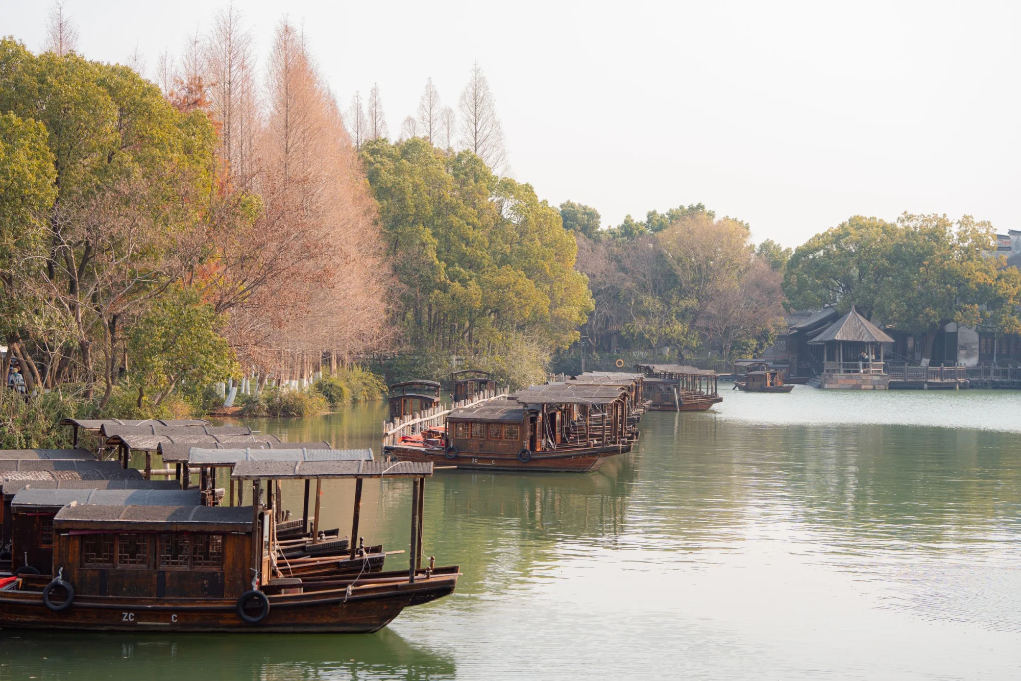 Wooden boats rest peacefully on a serene lake framed by lush trees in Hangzhou.