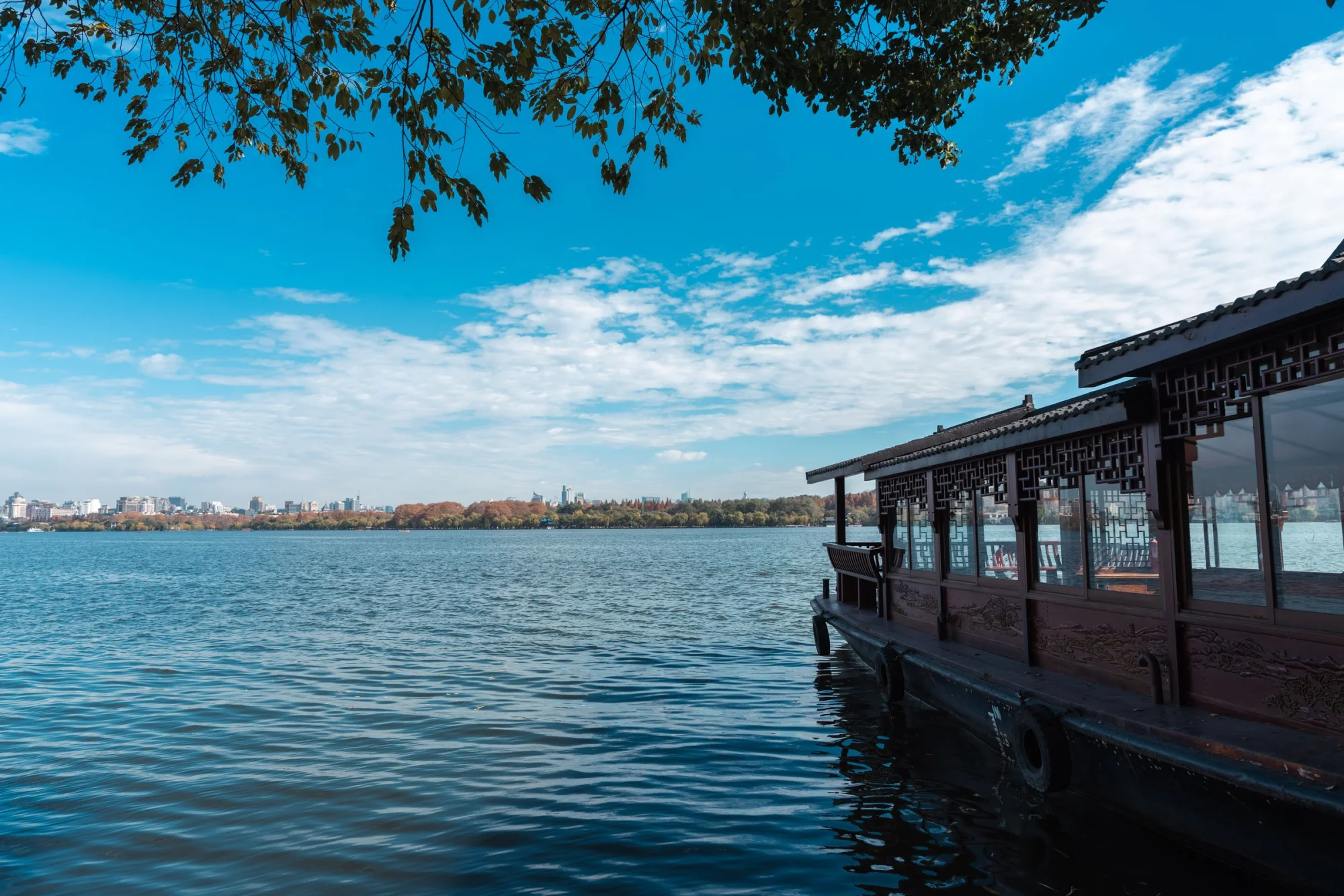 Serene view of a traditional boat on West Lake in Hangzhou, China, under clear blue skies.