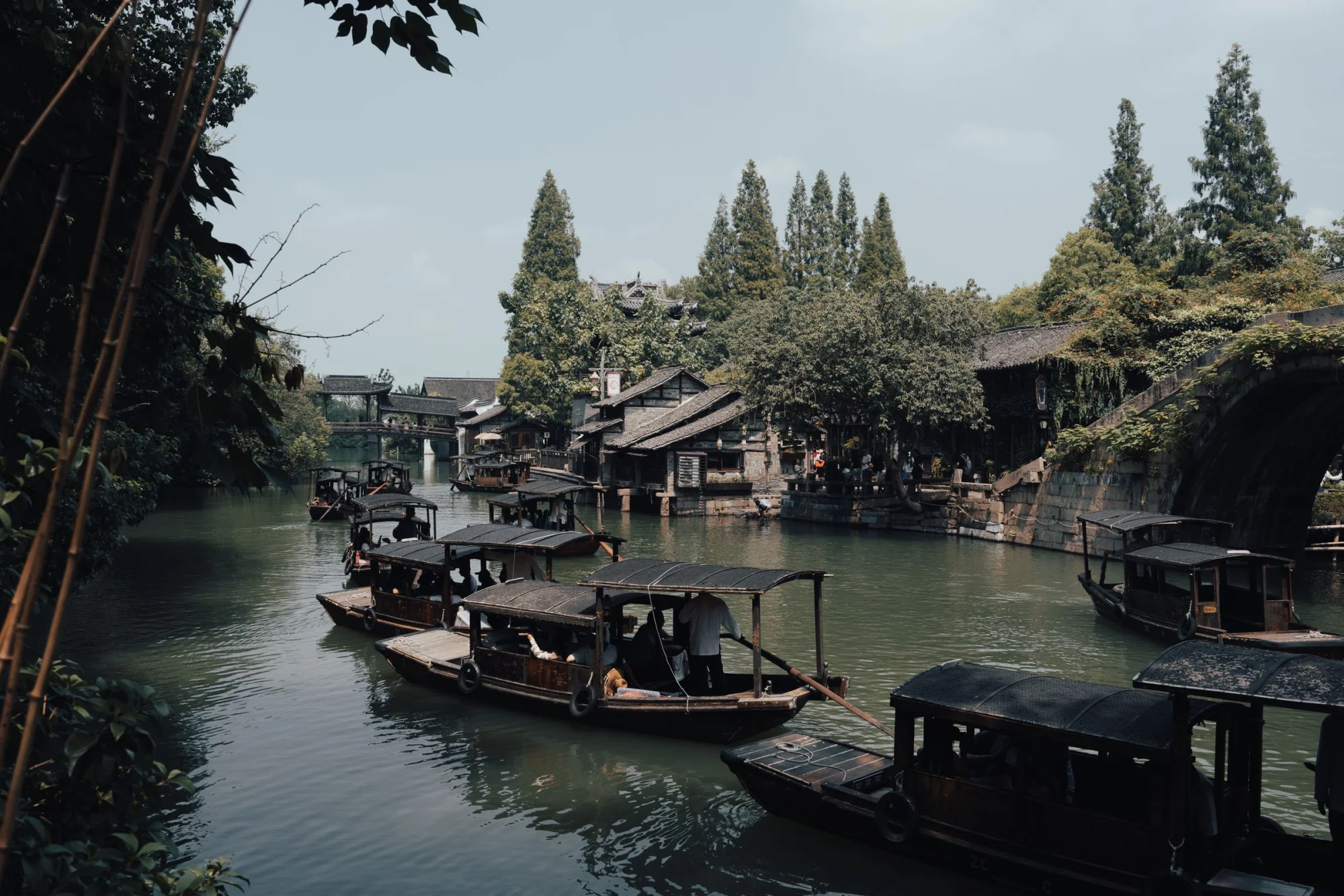 Serene river scene with traditional wooden boats in a scenic village surrounded by lush trees.
