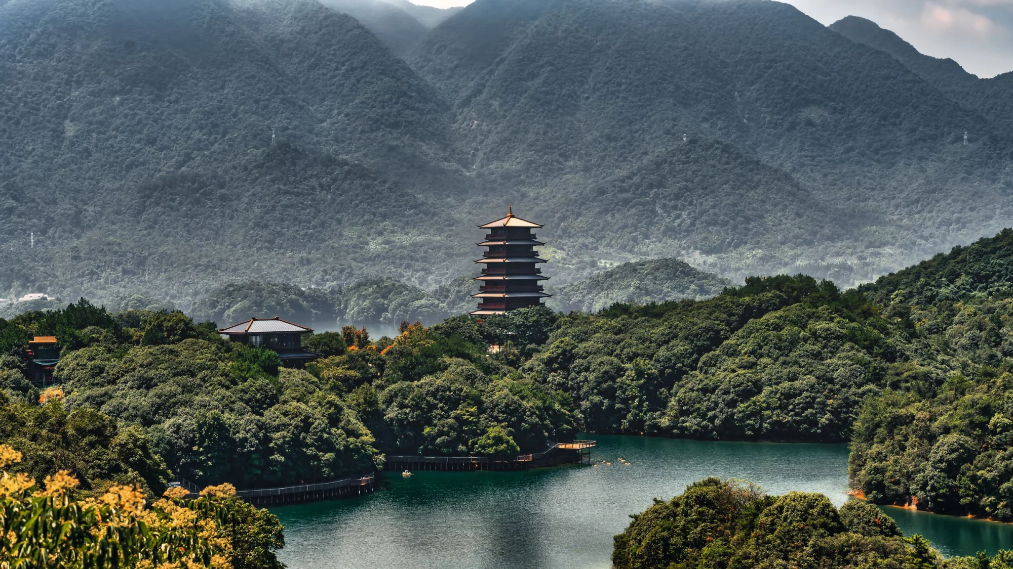 A pagoda rises above a dense forest with mountains in the background, creating a tranquil and picturesque scene.