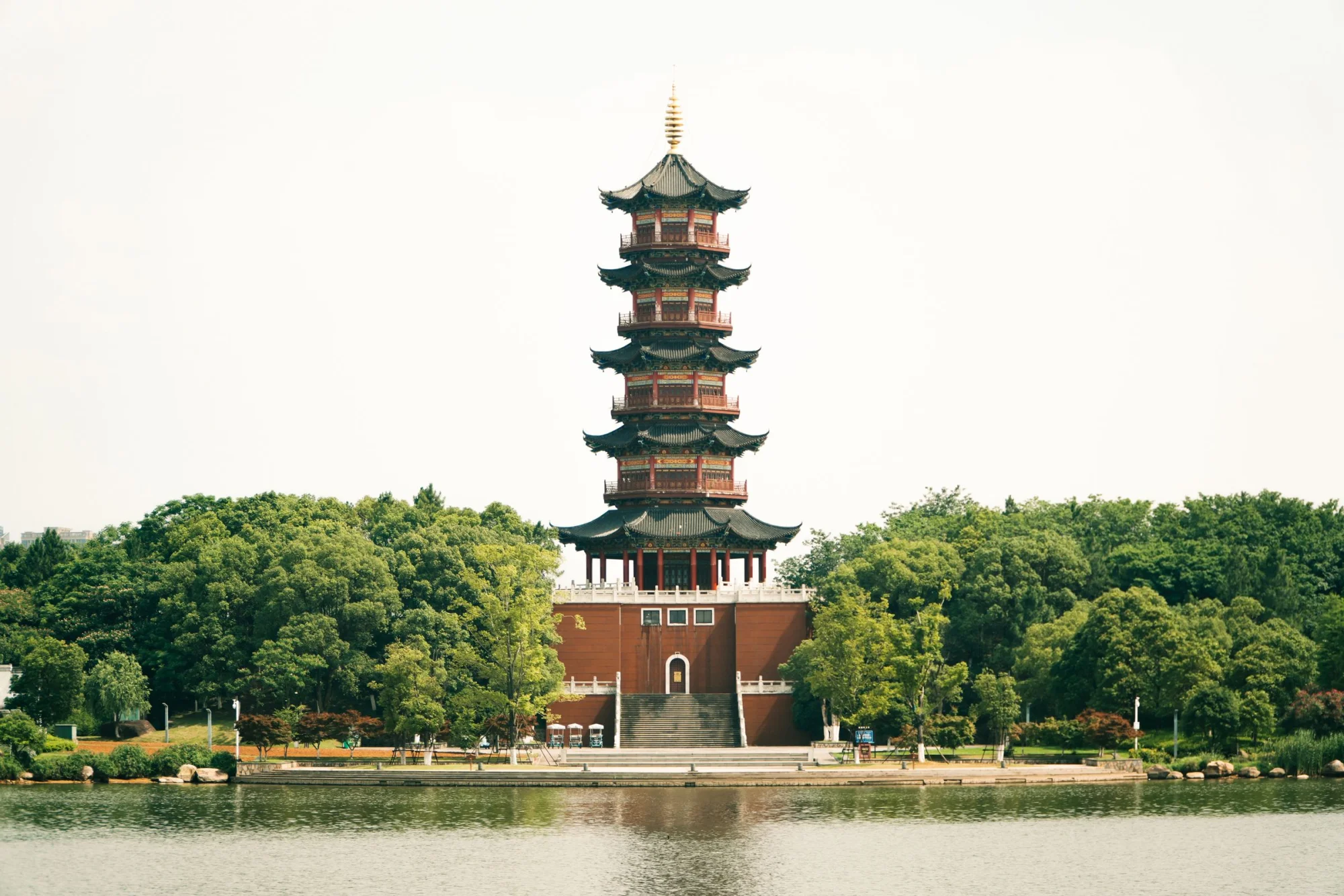 A beautifully serene view of an ancient pagoda surrounded by lush greenery and a tranquil lake.