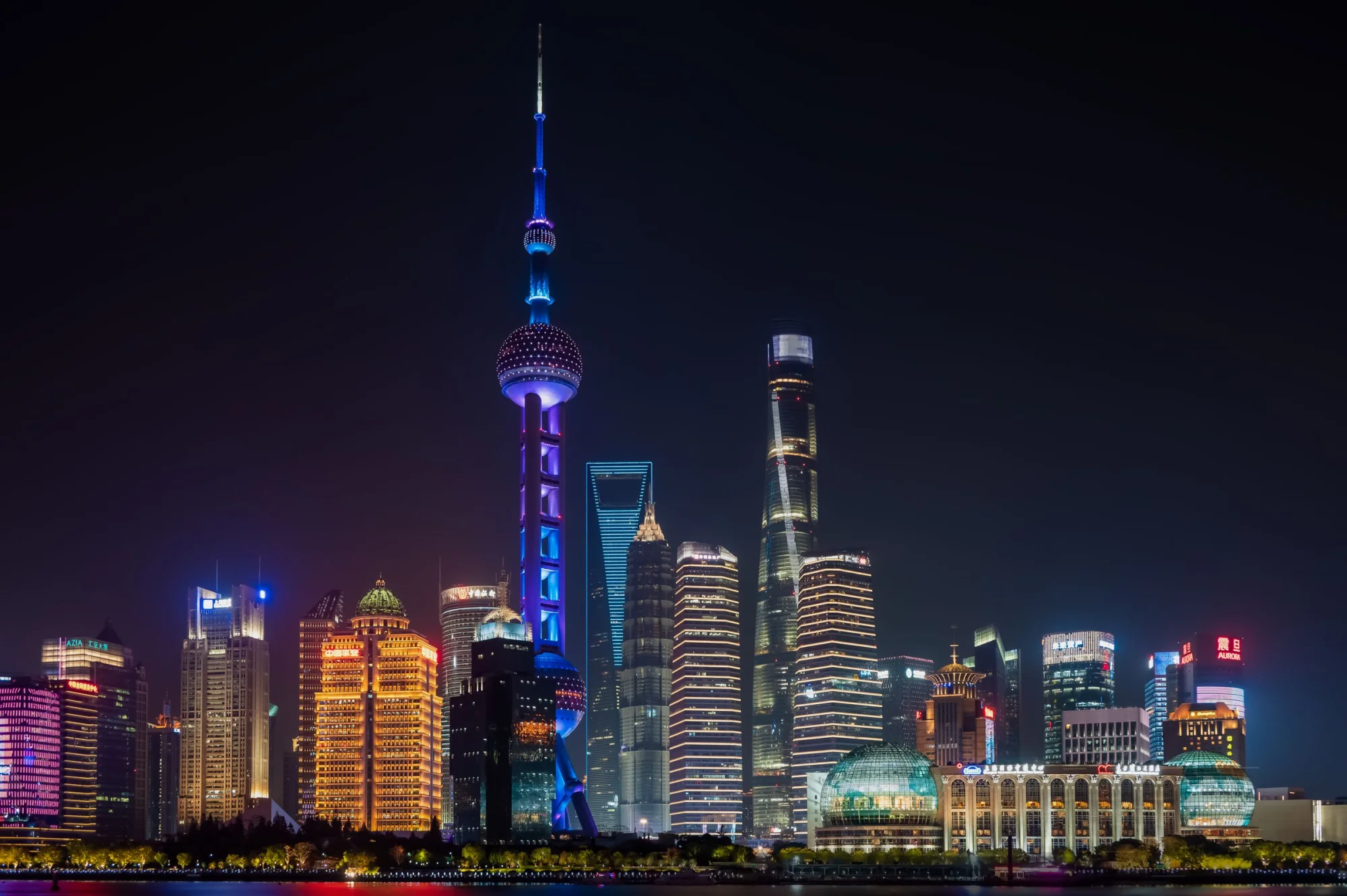 Illuminated Shanghai skyline featuring the Oriental Pearl Tower against a night sky.