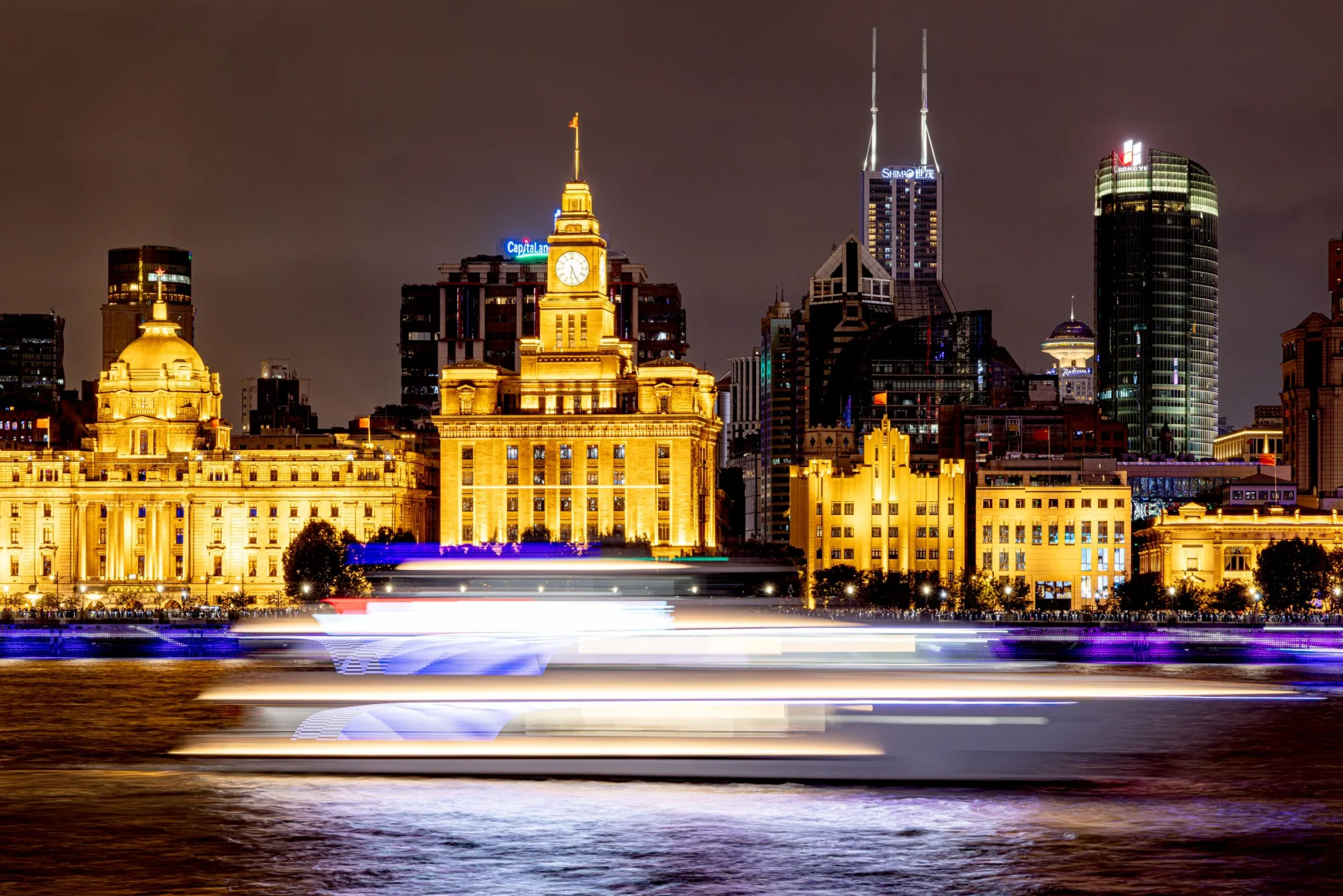 Shanghai's cityscape with The Bund and a passing boat lit up at night.