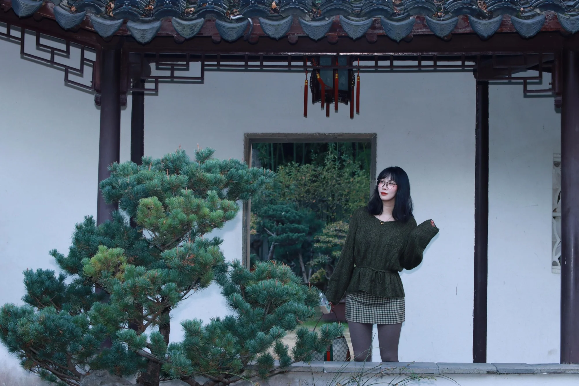 Woman standing in a traditional Chinese garden in Nanjing, China, wearing fashionable clothing.