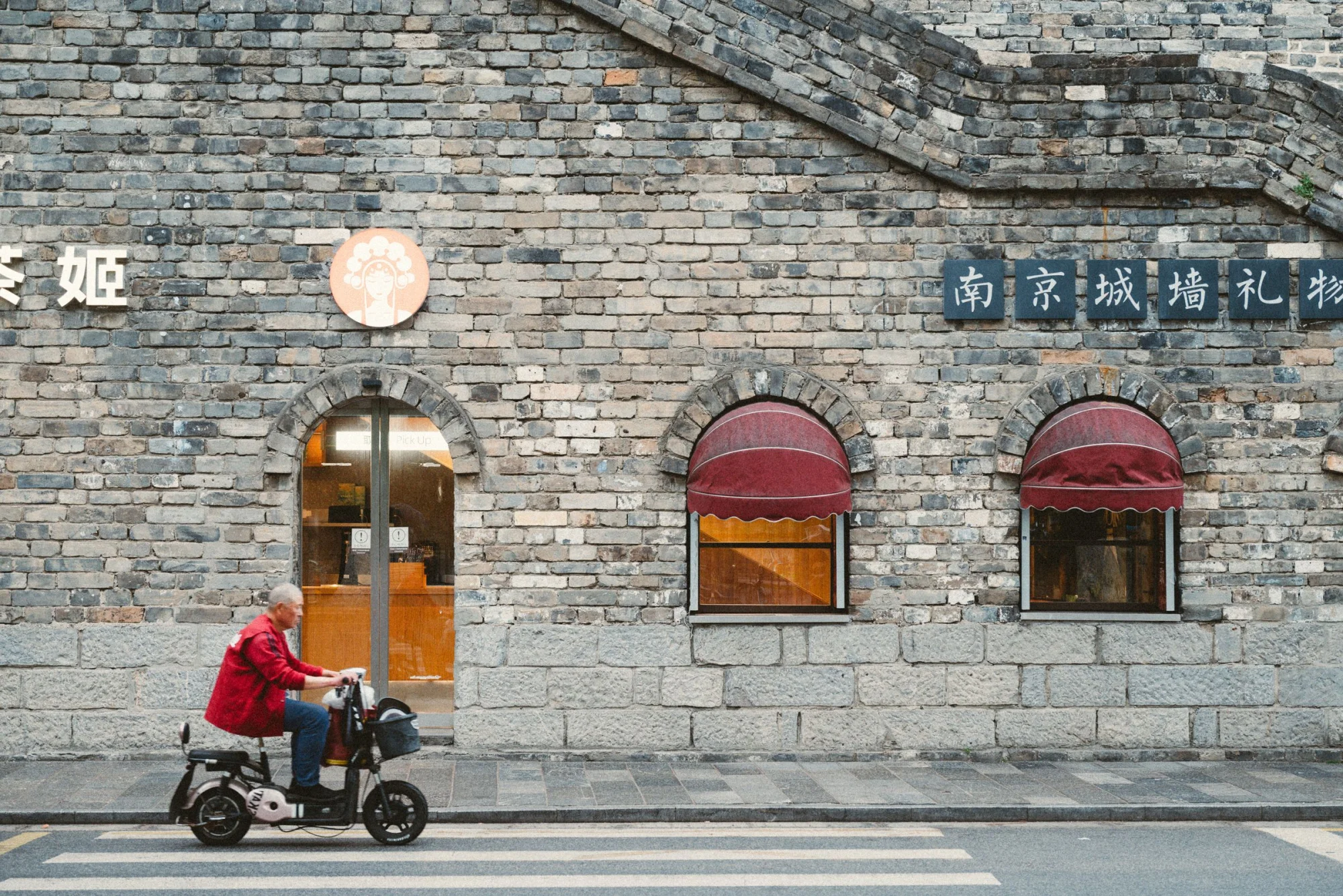 Man on electric scooter passes historic brick building with signage in Nanjing.