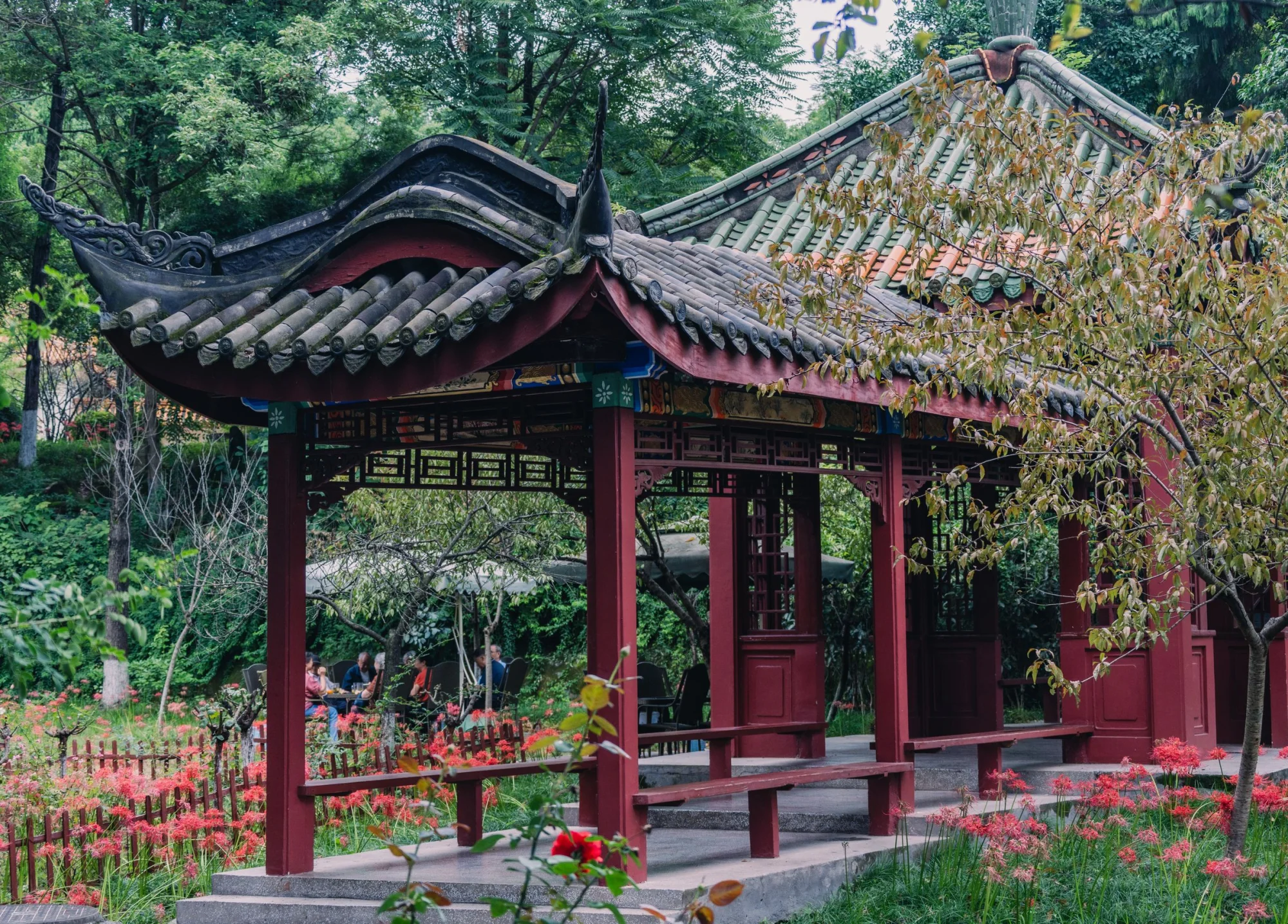Elegant Asian pavilion surrounded by lush greenery and vibrant flowers creating a serene outdoor atmosphere.
