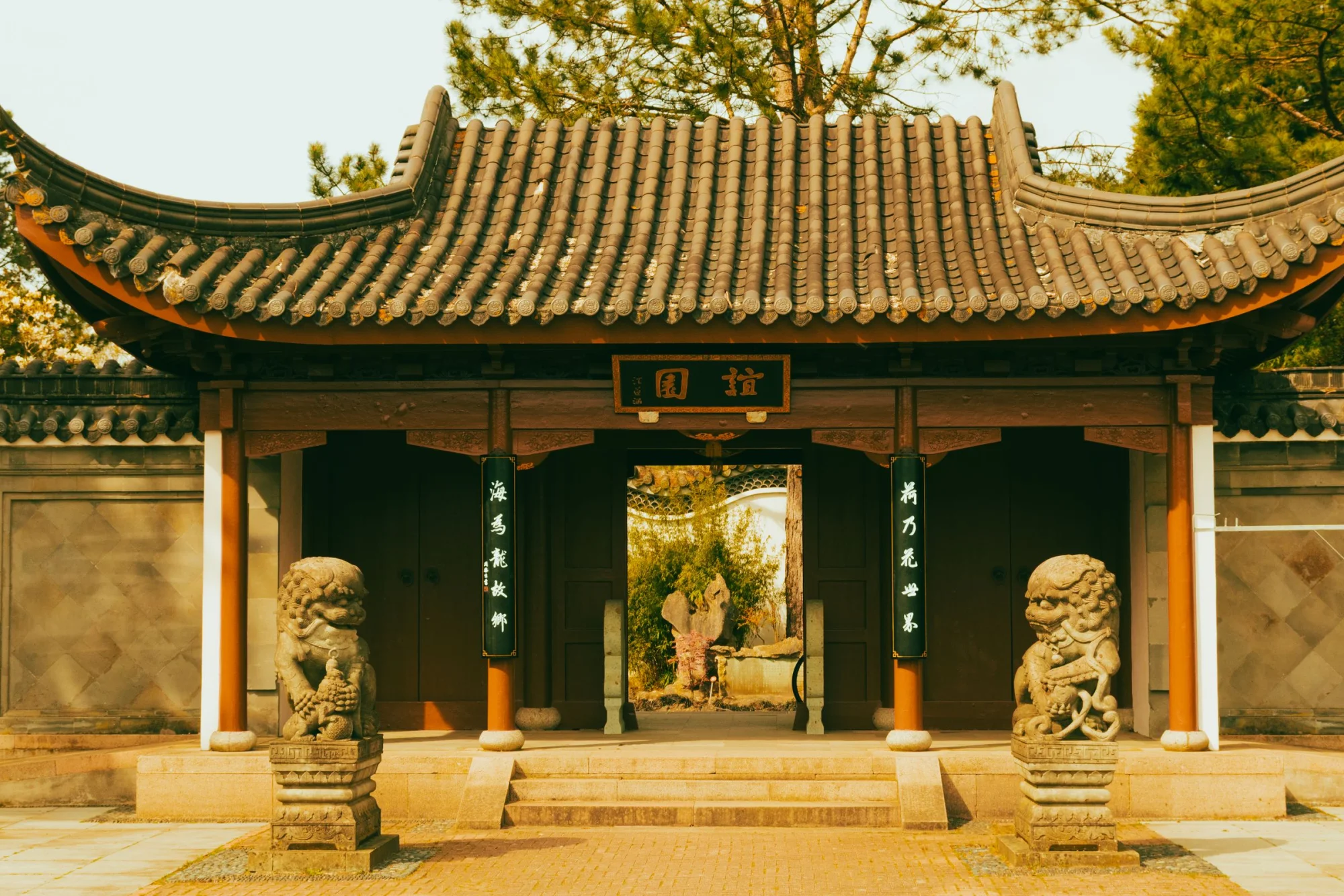 A traditional Chinese temple entrance adorned with stone lion statues under a warm daylight setting.
