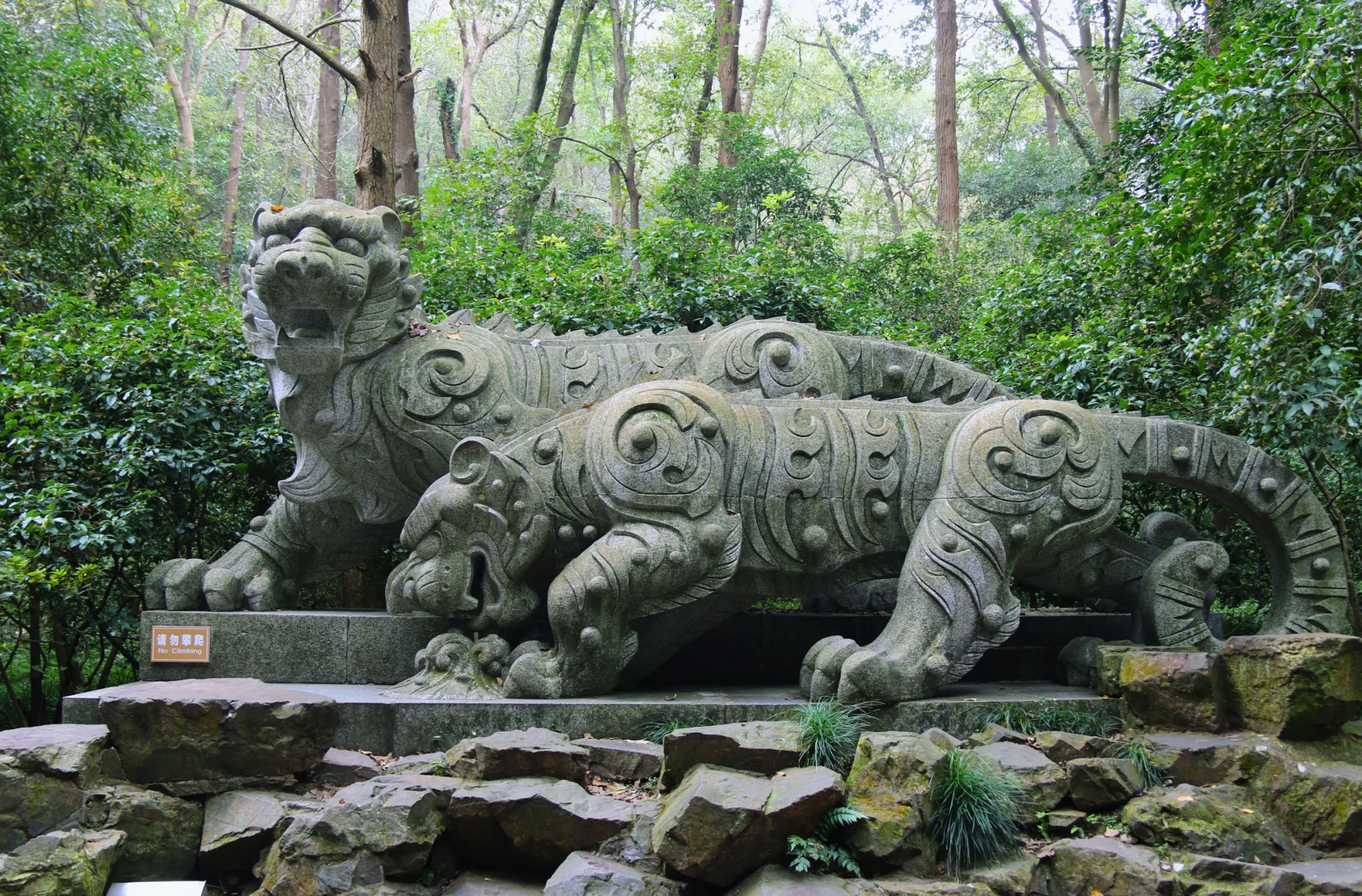 Intricate stone tiger sculptures in Hupao Park, Hangzhou, surrounded by lush greenery.