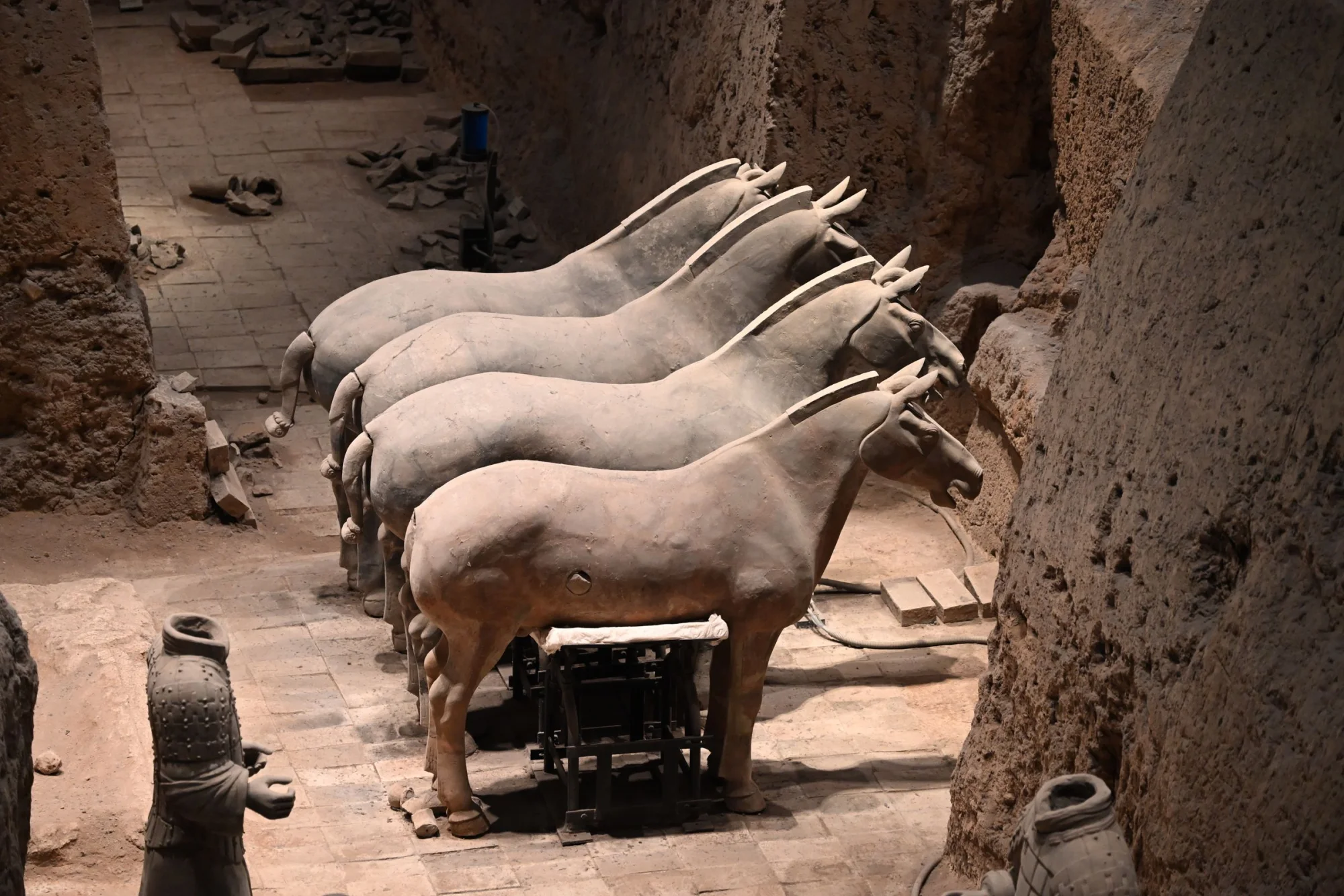 Row of ancient terracotta horse statues in a dimly lit archaeological site, revealing historical Chinese craftsmanship.