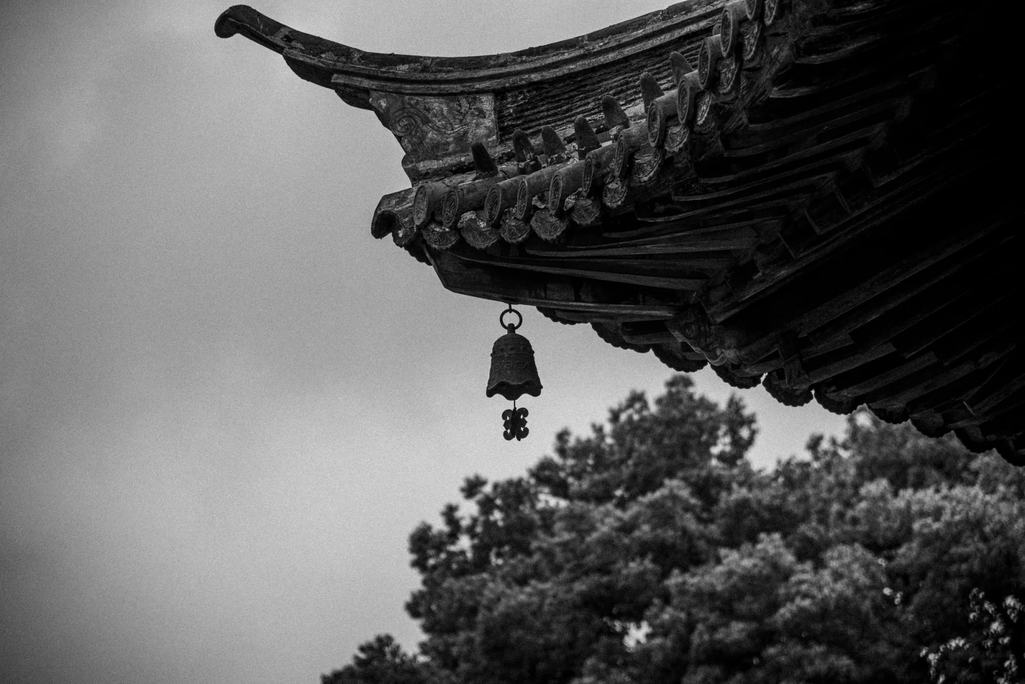 Close-up of a traditional temple roof with a hanging bell against a cloudy sky.