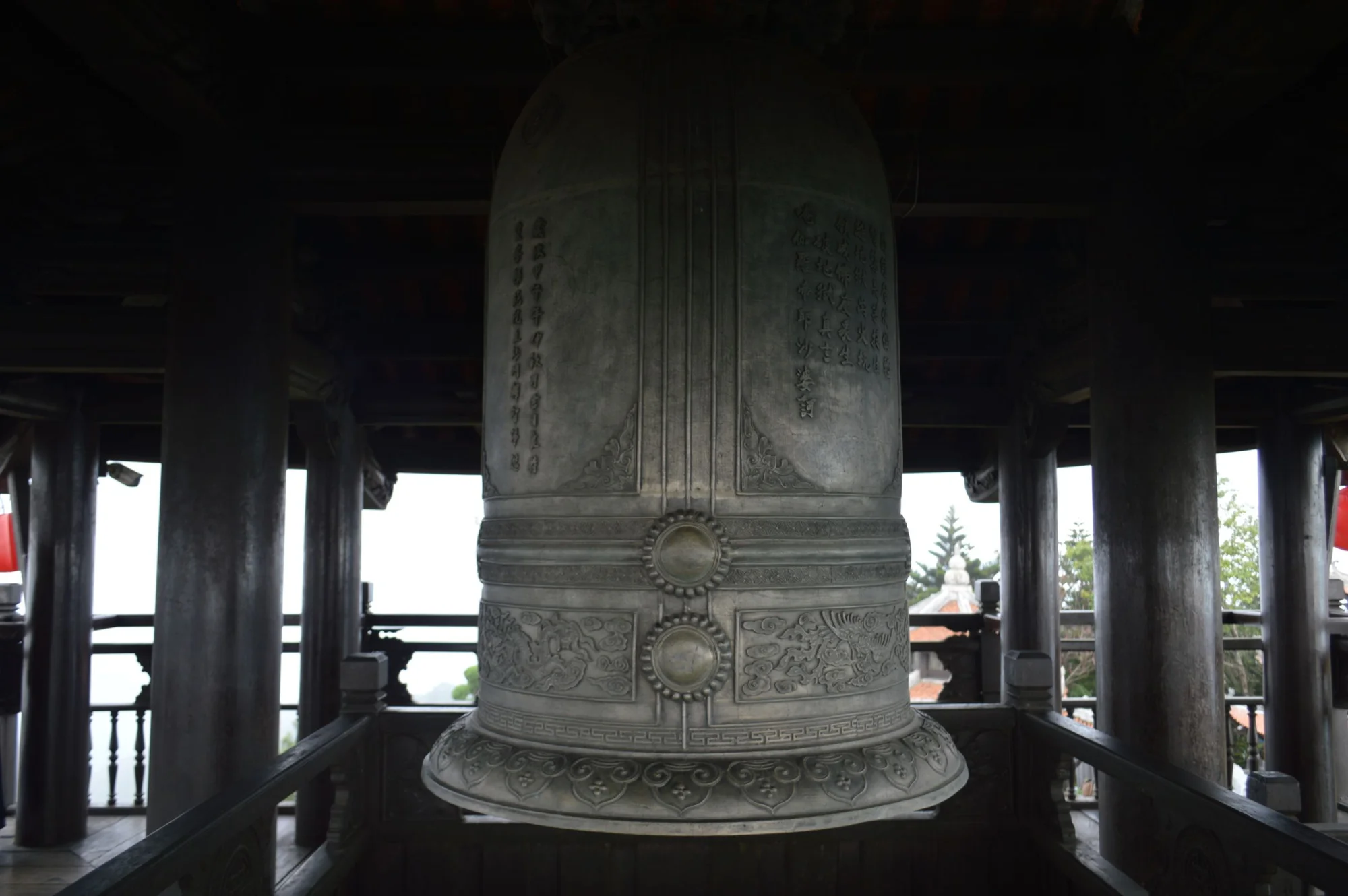 A large traditional metal bell inside an ancient wooden pagoda with artistic carvings.