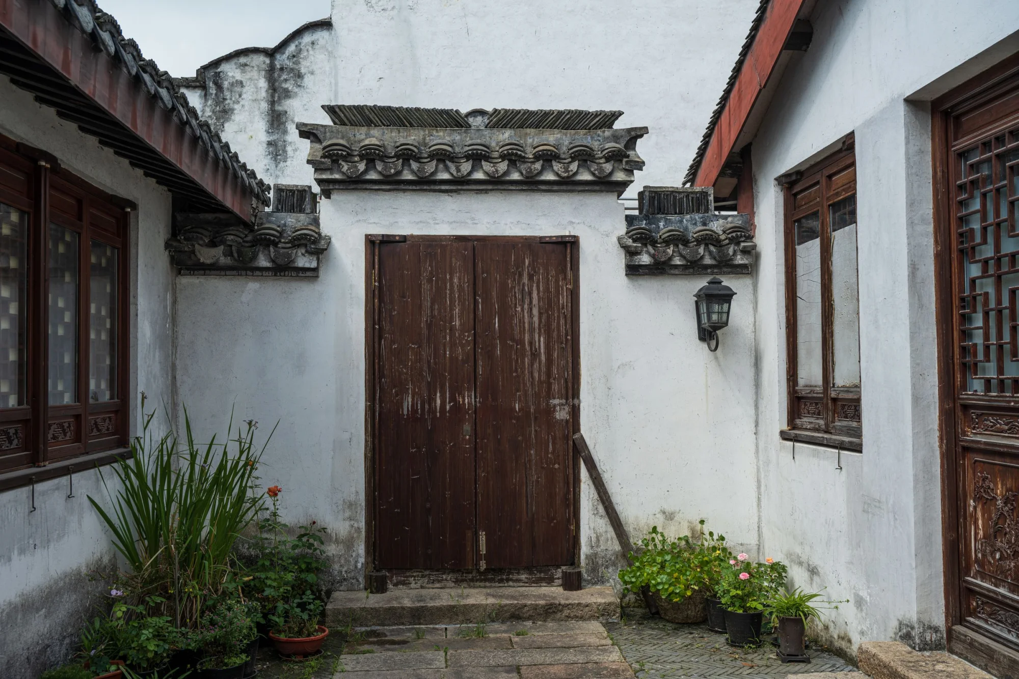 A serene traditional Chinese courtyard with a weathered wooden door and potted plants.