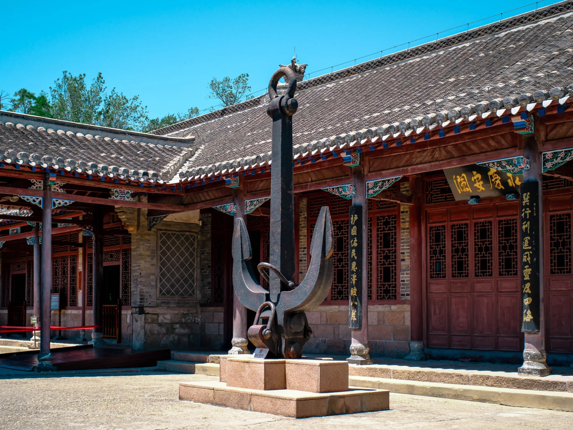 A traditional Asian courtyard featuring an anchor sculpture and wooden buildings on a sunny day.