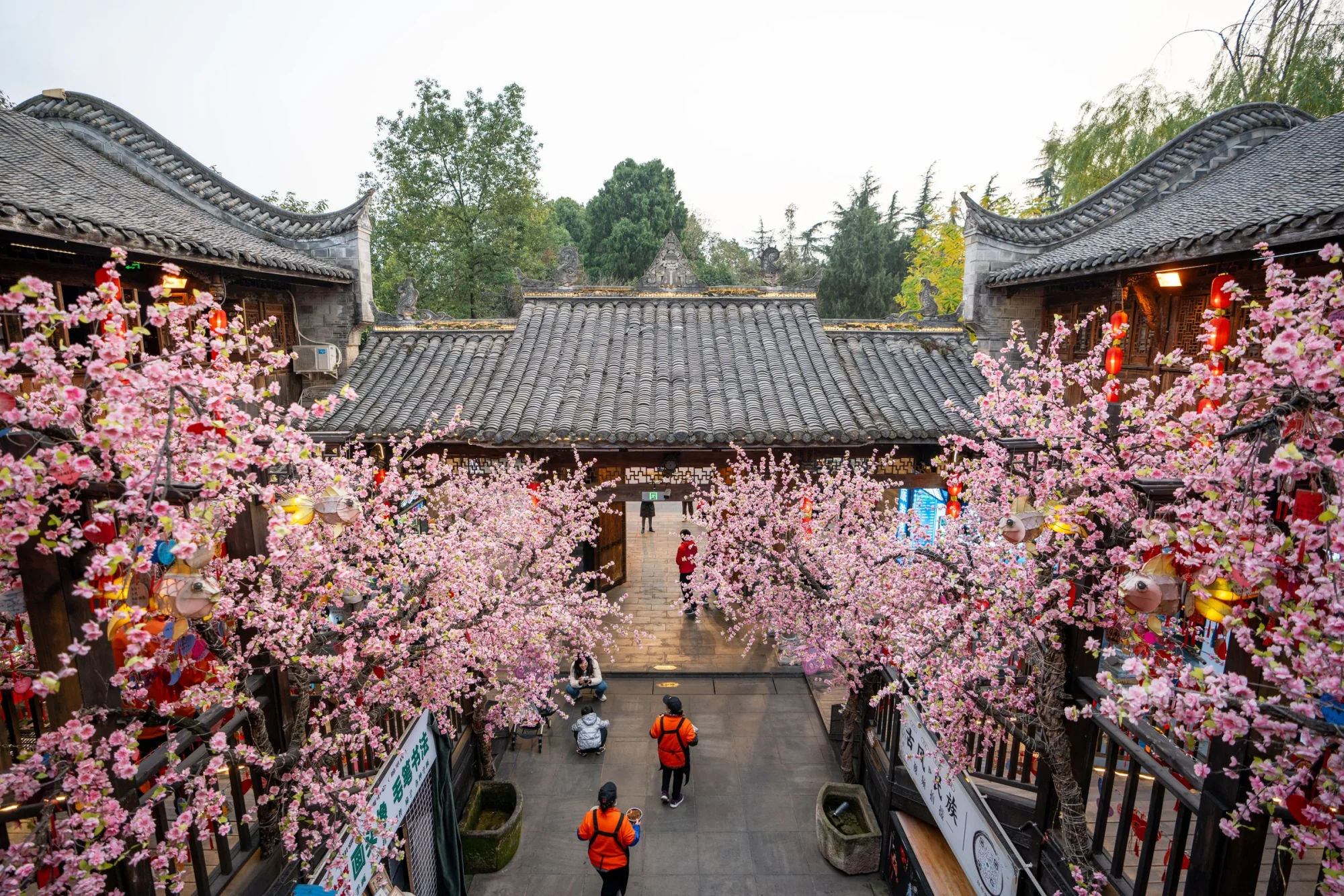 A vibrant scene of traditional Asian architecture adorned with cherry blossoms in a bustling courtyard.