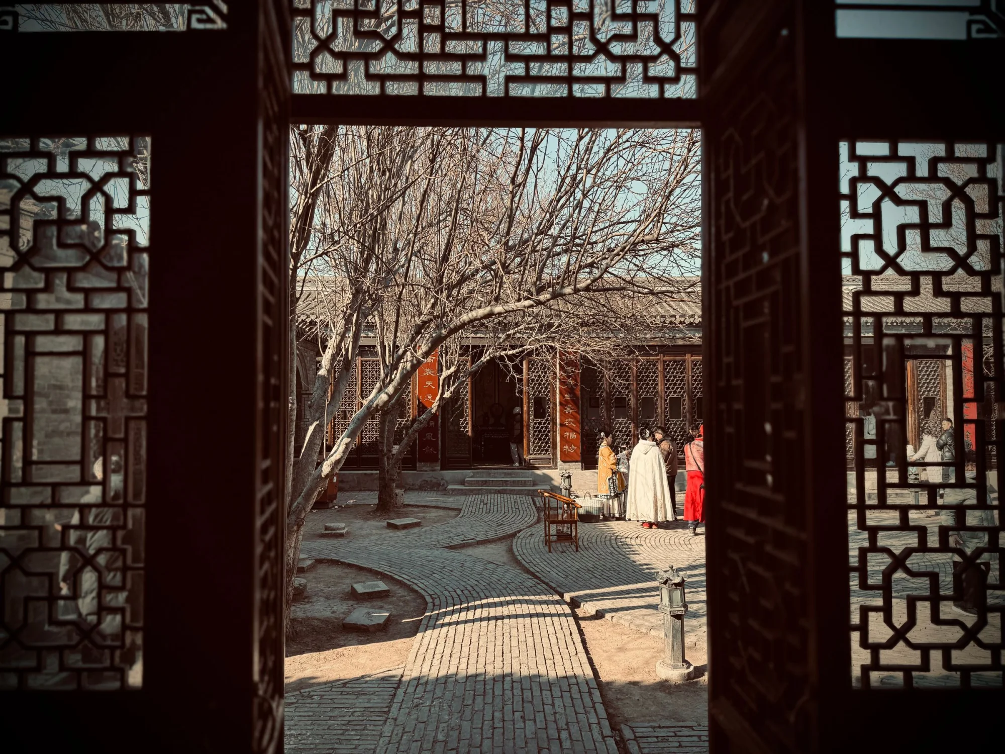 Elegant view of a traditional courtyard through ornate wooden windows, showcasing historical architecture and cultural charm.